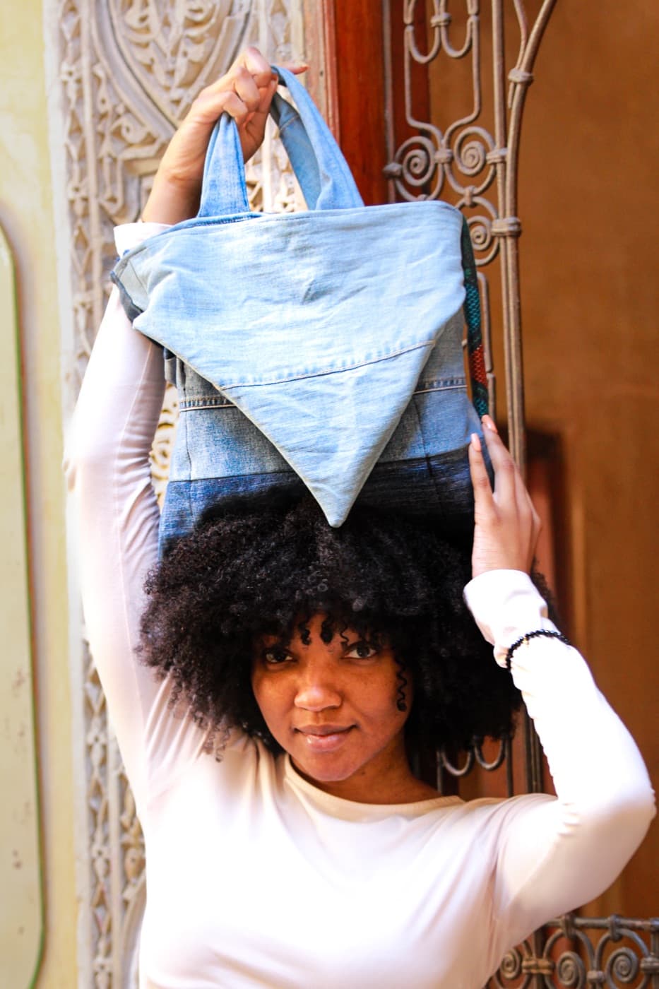A woman holding a SamZar denim bag aloft above her head, facing the camera with a steady gaze.