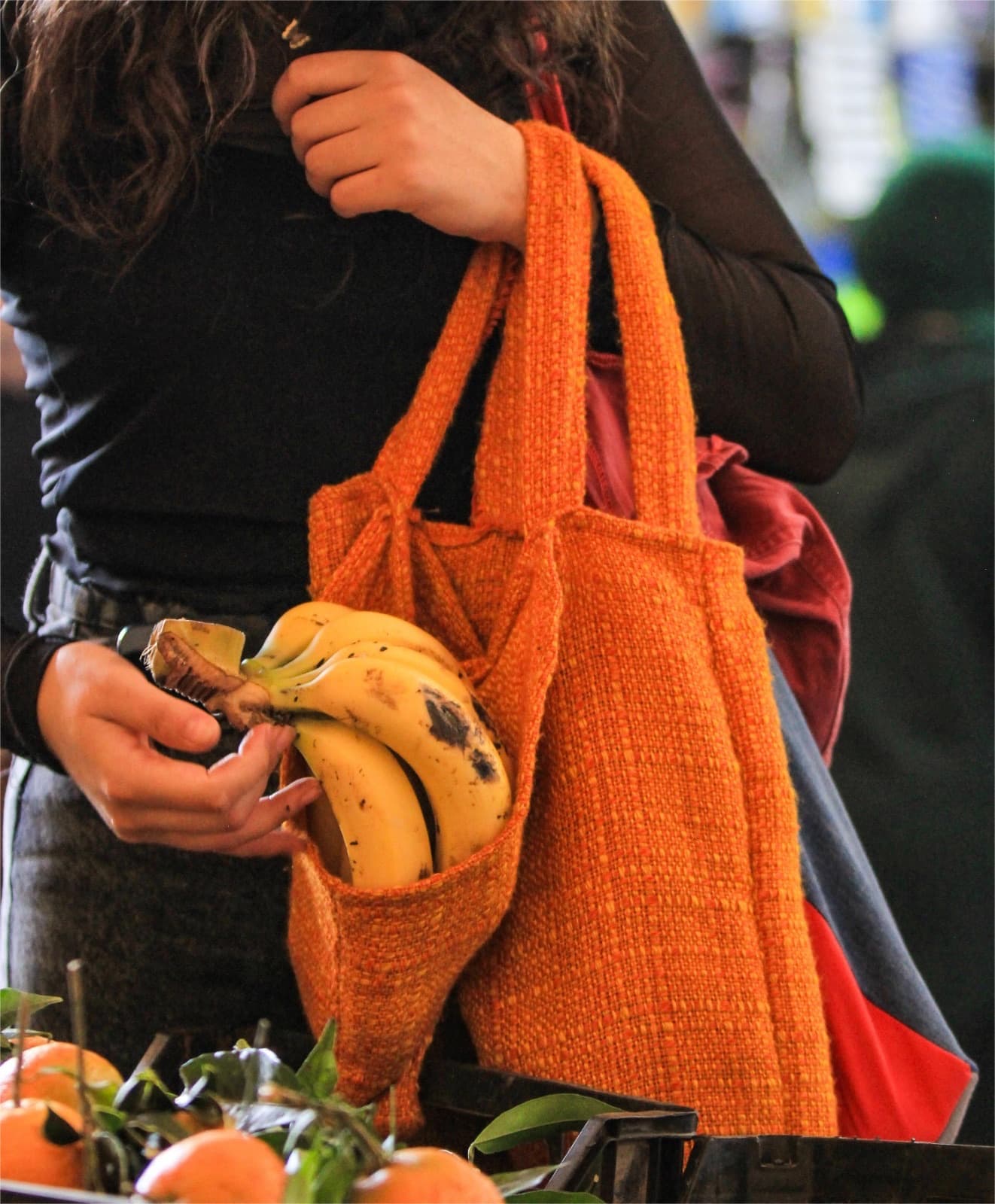 An orange knitted Medina Bag carrying bananas through a Fez market.