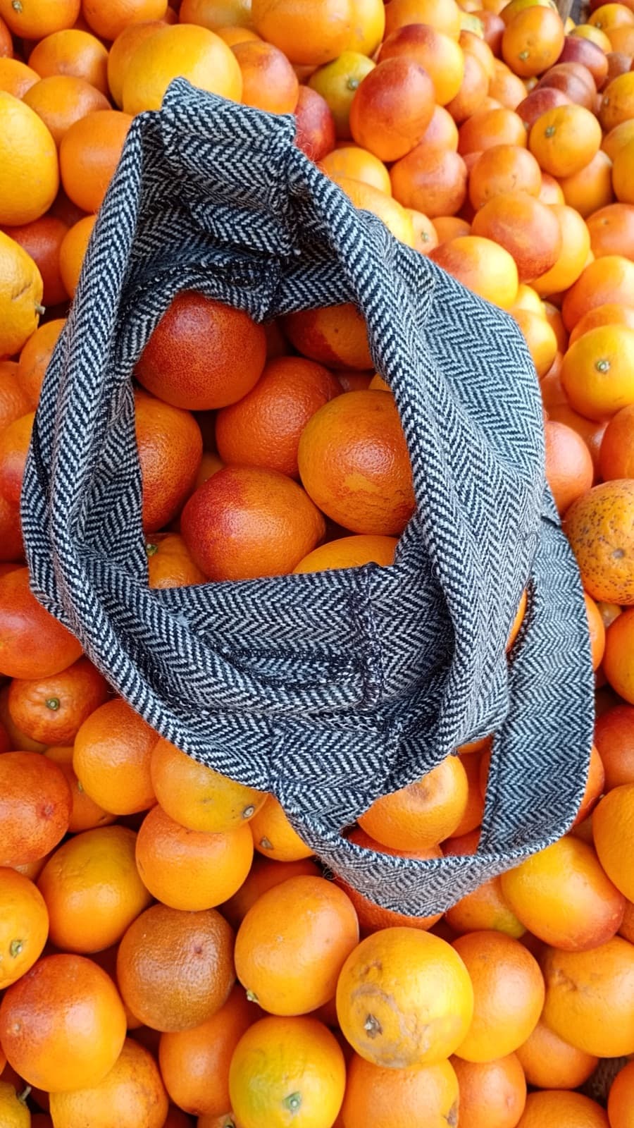 A herringbone Soft Fruit Bag resting on a market crate of oranges.
